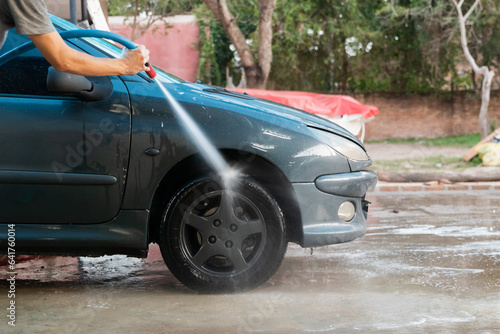Man holding a hose, washing the front wheel of a car.