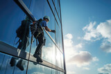 Backview of a high - rise window cleaner in sunlight. A male industrial climber washes the windows of a tall modern skyscraper. 