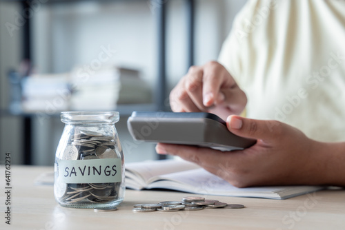 A woman' calculating and placing coins into a glass jar, the act of saving money to pay bills.