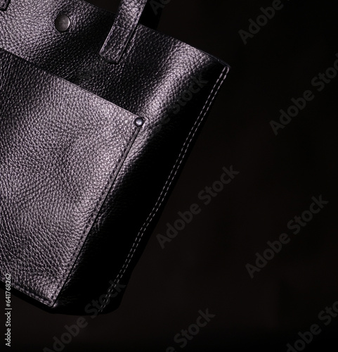 Fragment of a black leather bag on a black background