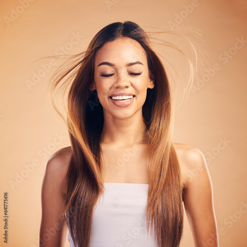 Face, hair and wind with an aesthetic woman in studio on a brown background for shampoo treatment. Smile, beauty and keratin with a happy young model at the salon for growth or natural haircare