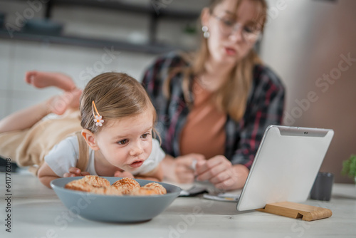 One young woman with toddler girl in the kitchen making a video call and playing with finger puppets  babysitting at home concept
