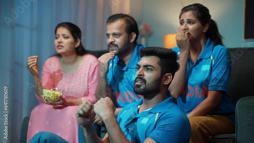 Senior Middle aged parents with siblings watching live Cricket sports match with Indian Tshirts at home on sofa - concept of entertainment, Nail biting and intense expression. photo