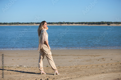 Beautiful young blonde woman walks on the sand of the beach on the south coast of spain in Sanlucar de barrameda, city of wine and gastronomy, in the background river mouth and national park