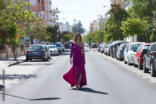 Fotografi Young beautiful blonde woman dressed in purple dress walks along a large lonely avenue among the stopped cars