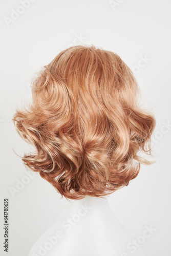Natural looking blonde fair wig on white mannequin head. Short hair cut on the plastic wig holder isolated on white background, back view.
