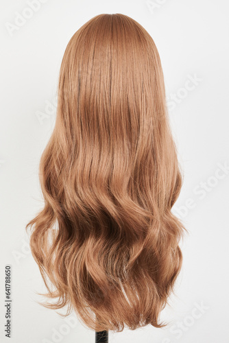 Natural looking dark blonde wig on white mannequin head. Long fair hair cut on the plastic wig holder isolated on white background