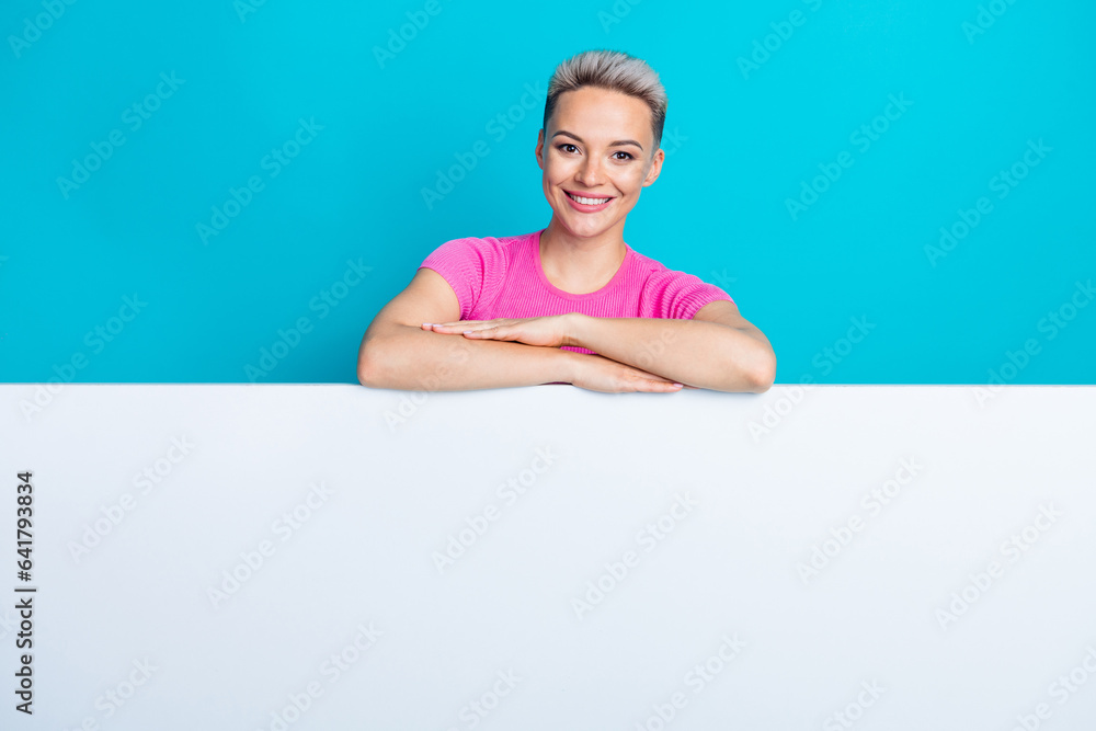 Photo of gorgeous good mood girl short haircut dressed pink t-shirt hands hold arms on board empty space isolated on blue color background Photo of gorgeous good mood girl short haircut dressed pink t-shirt hands hold arms on board empty space isolated on blue color background