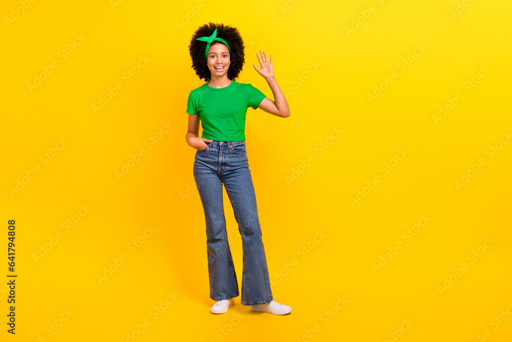 Fototapeta premium Full length portrait of friendly cute cheerful girl arm palm waving hi empty space ad isolated on yellow color background