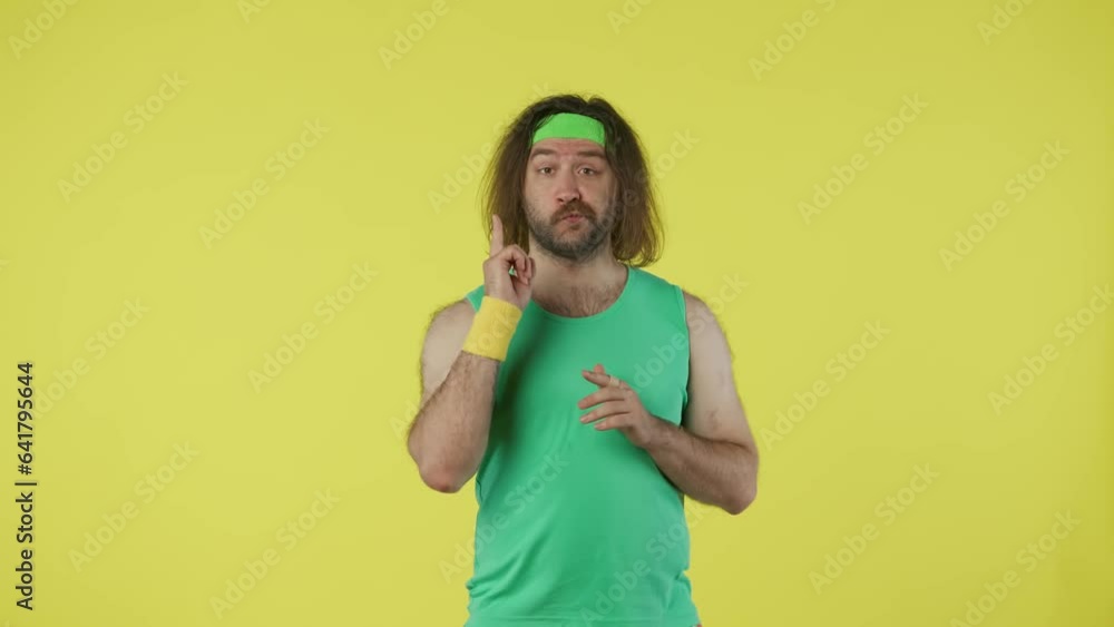 Man in green top and headband thinking about something, coming up with an idea pointing finger. Isolated on yellow background. Man in green top and headband thinking about something, coming up with an idea pointing finger. Isolated on yellow background.