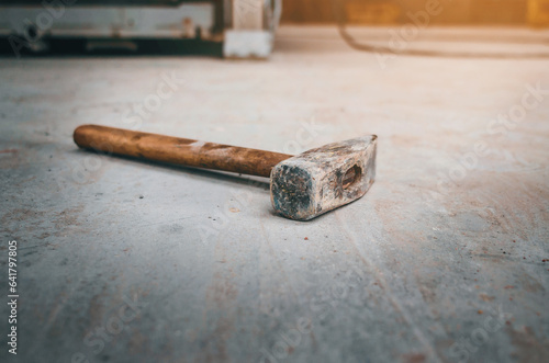 An old hammer with wooden handle lies on a concrete floor