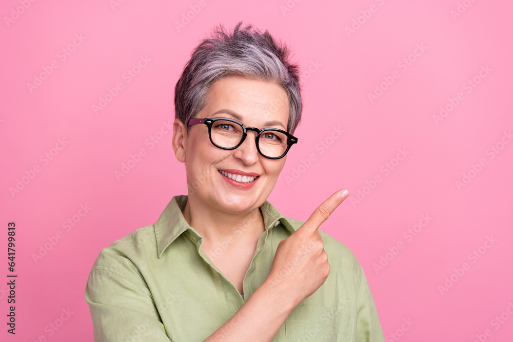 Photo of satisfied senior businesswoman khaki shirt directing finger empty space advertisement vacancy isolated on pink color background
