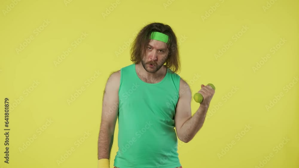 Man in green top and headband holding dumbbell doing exercise for biceps, looking at the camera smiling. Isolated on yellow background. Man in green top and headband holding dumbbell doing exercise for biceps, looking at the camera smiling. Isolated on yellow background.