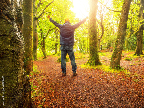 Man standing with hands up at a forest autumn park on a warm sunny day. Outdoor activity for relaxation and energizing mind and body. Active lifestyle. Beautiful nature background.