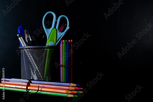 Crayons, Pencil colors, and a scissor with pen stand shot against black background -Student Life concept. photo