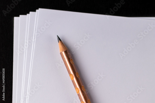 High angle close up shot of a pencil placed diagonally over white papers in elementary educaiton concept.