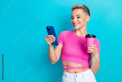 Photo portrait of pretty young girl hold telephone paper cup takeout comment dressed stylish pink outfit isolated on cyan color background