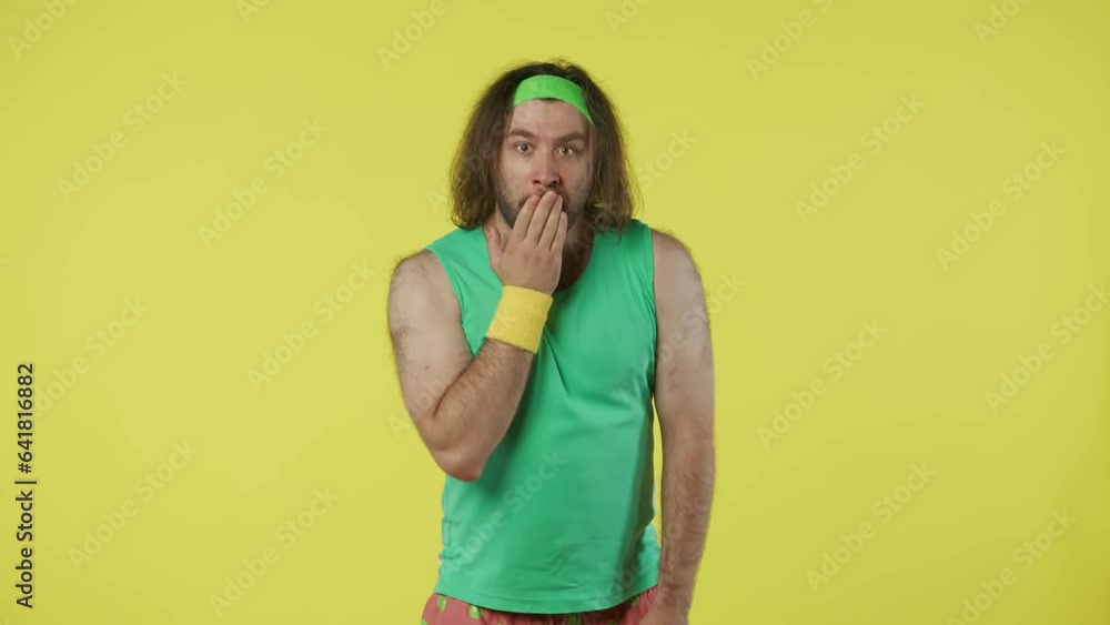 Man in green top and headband looking directly at the camera with shocked, surprised face. Isolated on yellow background. Man in green top and headband looking directly at the camera with shocked, surprised face. Isolated on yellow background.