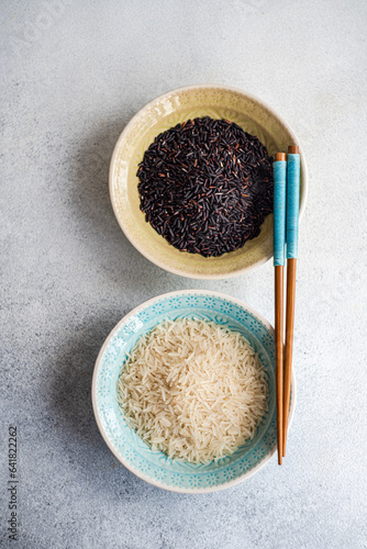 Raw wild black rice and peeled white rice in the bowls with chopsticks. photo