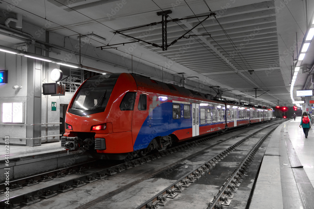 Red and blue passenger train at the platform of railway station. Commuter train is ready to departure from railway station