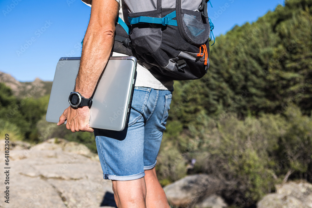 © ADDICTIVE STOCK - Anonymous man with laptop and backpack on cliff