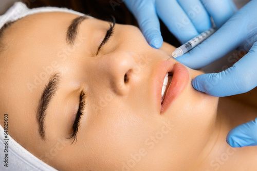 Young beautiful woman gets injection of botox in her lips for lip augmentation by cosmetologist in beauty salon  photo