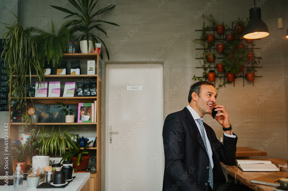 Businessman standing at the bar table in a cafe and talking on his cell phone Businessman standing at the bar table in a cafe and talking on his cell phone