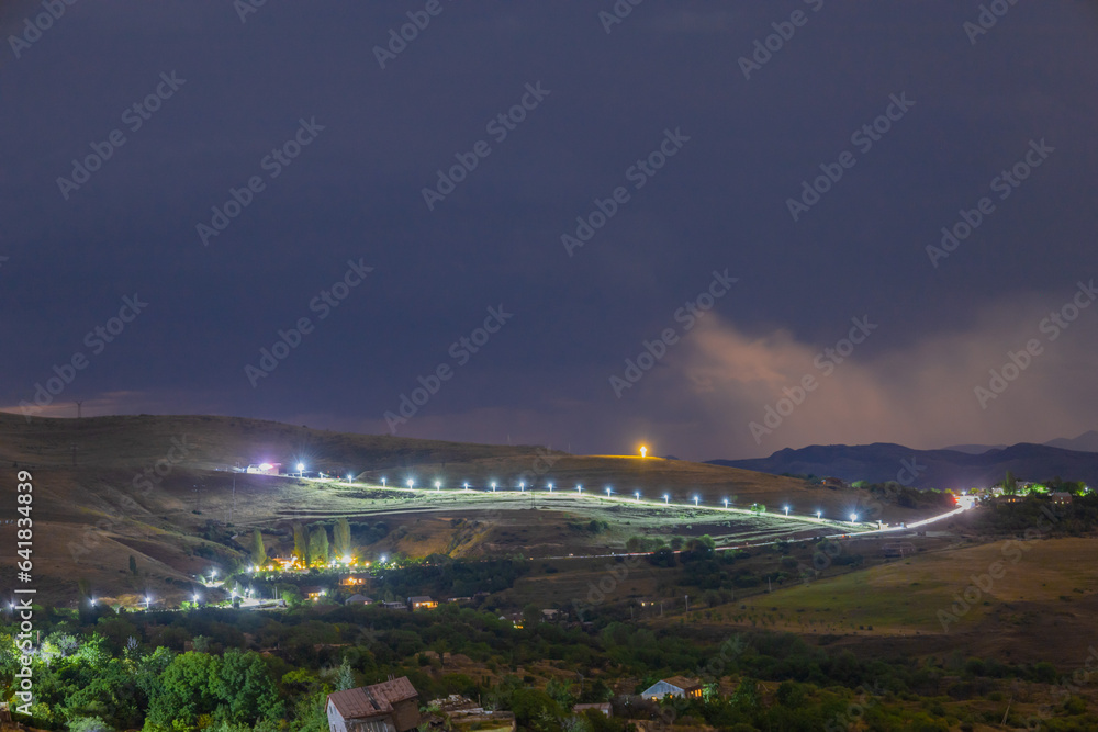 Long distance shot of a village and a brightly lit road in the highlands in the evening, Yerevan-Garni highway