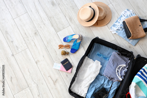 Open suitcase with beach accessories on light wooden floor, top view