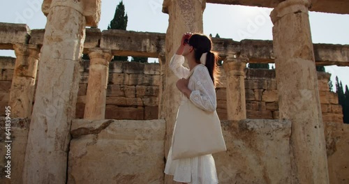 Woman in a white dress and sunglasses journey through the antiquated ruins of streets of Hierapolis, Turkey