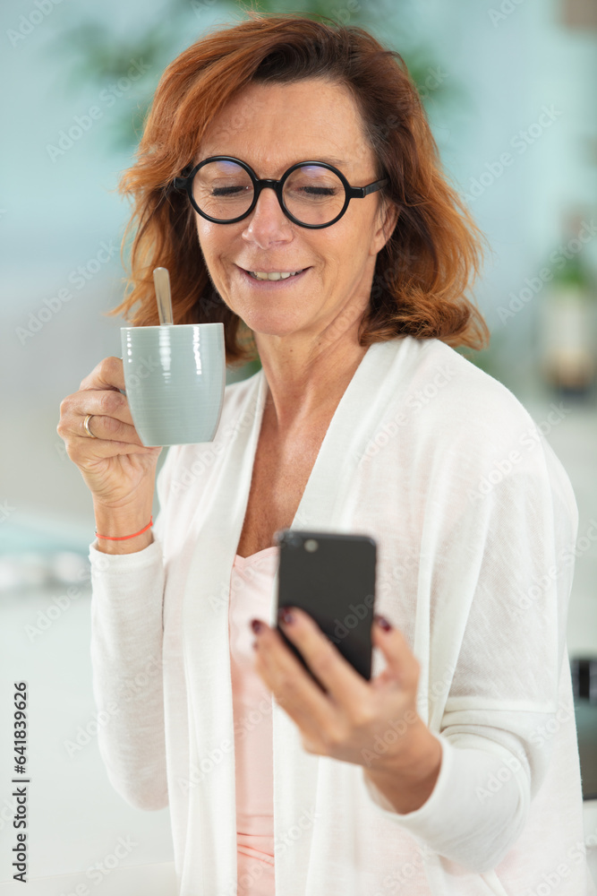 mature woman holding coffee and looking at smartphone mature woman holding coffee and looking at smartphone