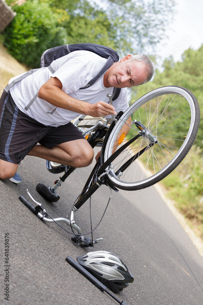 Fototapeta premium mature man repairing bicycle outdoors on tarmac surface