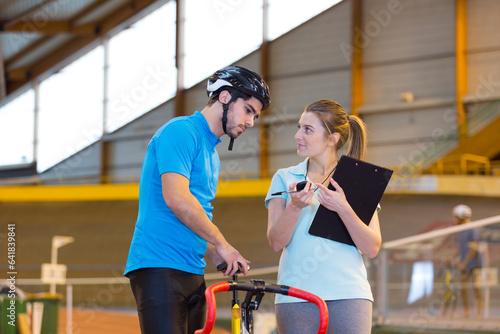 trainer woman talking with a man doing exercise bike