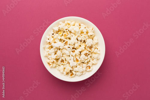 Tasty popcorn in bowl on color background, top view