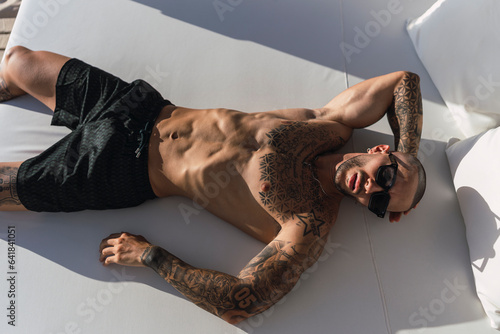 Chico joven tatuado y musculoso posando en verano en playa soleada