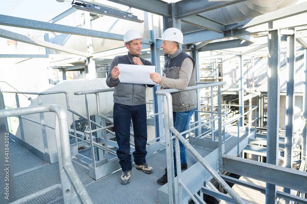 workers on platform of industrial site looking at paperwork workers on platform of industrial site looking at paperwork