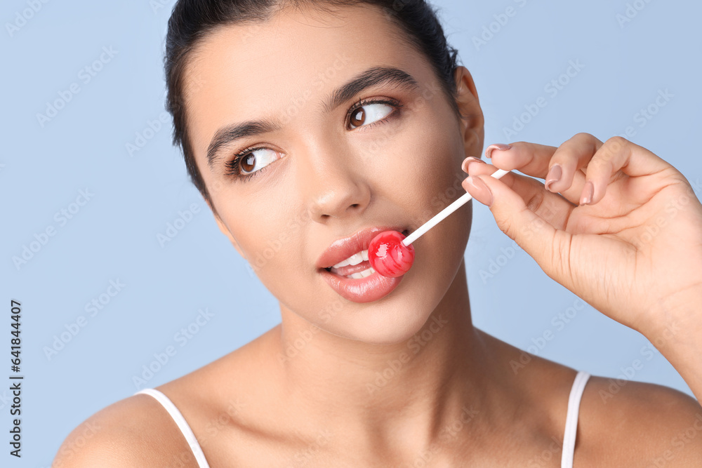 Young woman with beautiful lips eating lollipop on blue background, closeup Young woman with beautiful lips eating lollipop on blue background, closeup