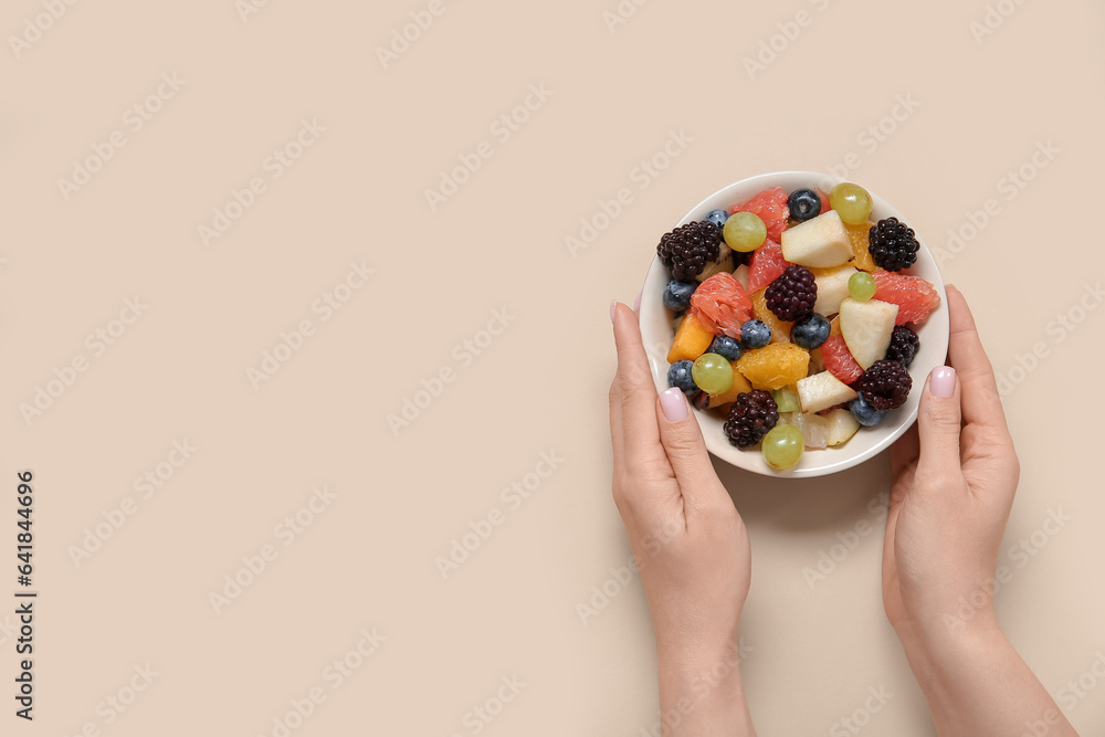 Woman with bowl of fresh fruit salad on beige background Woman with bowl of fresh fruit salad on beige background
