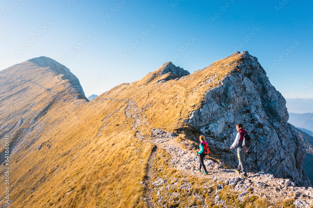 Canvas Print Couple trekking, walking uphill with a great view of the mountain range in the background