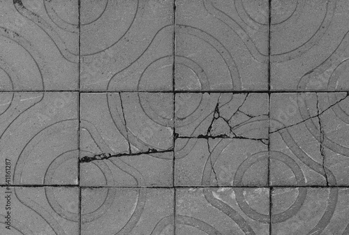 Broken and weathered square paving stones or blocks with geometric shapes outdoors, viewed from above. High resolution full frame textured background in black and white.