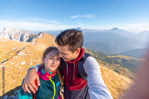 Happy hiking couple taking selfie and walking up mountain ridge on a sunny autumn day. Life motivation, inspiration, effort, and tenacity concepts.