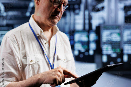 Senior supervisor inspects operational server rigs in computer network security data center, ensuring errorless performance. Trained expert monitoring energy consumption across hardware parts photo