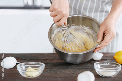 A cook in an apron kneads the dough in a bowl using a whisk for baking bread, dessert, pie, buns. Homemade or handmade bread, dessert. Kitchen background.
