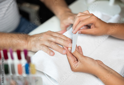 Skilled hands of professional young female manicurist delicately shaping and polishing nails to male client in salon, cropped shot