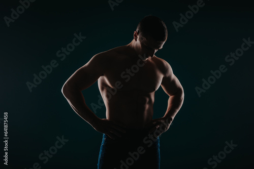 Fit male sports person posing in studio. He is looking at his abs.