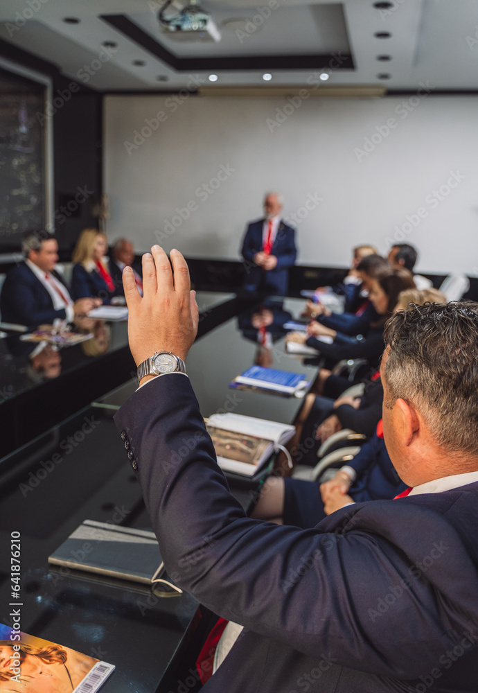 Businessman raising hand to ask question his elderly trainer during meeting in modern conference room. Businessman raising hand to ask question his elderly trainer during meeting in modern conference room.