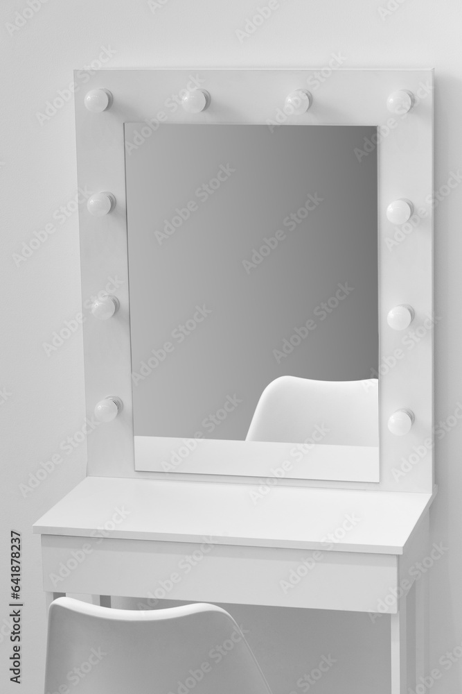 White makeup dressing table with lamps and a chair against a white wall, close-up White makeup dressing table with lamps and a chair against a white wall, close-up