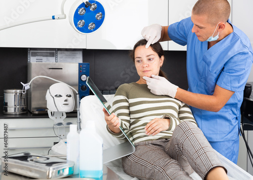 Male beautician in gloves examining face skin of young woman before procedure at cosmetology clinic