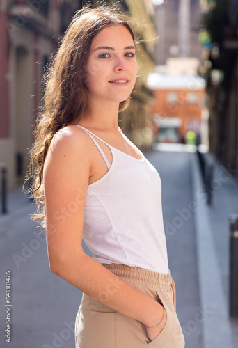 Cheerful attractive female is walking in white jersey on the street outdoor