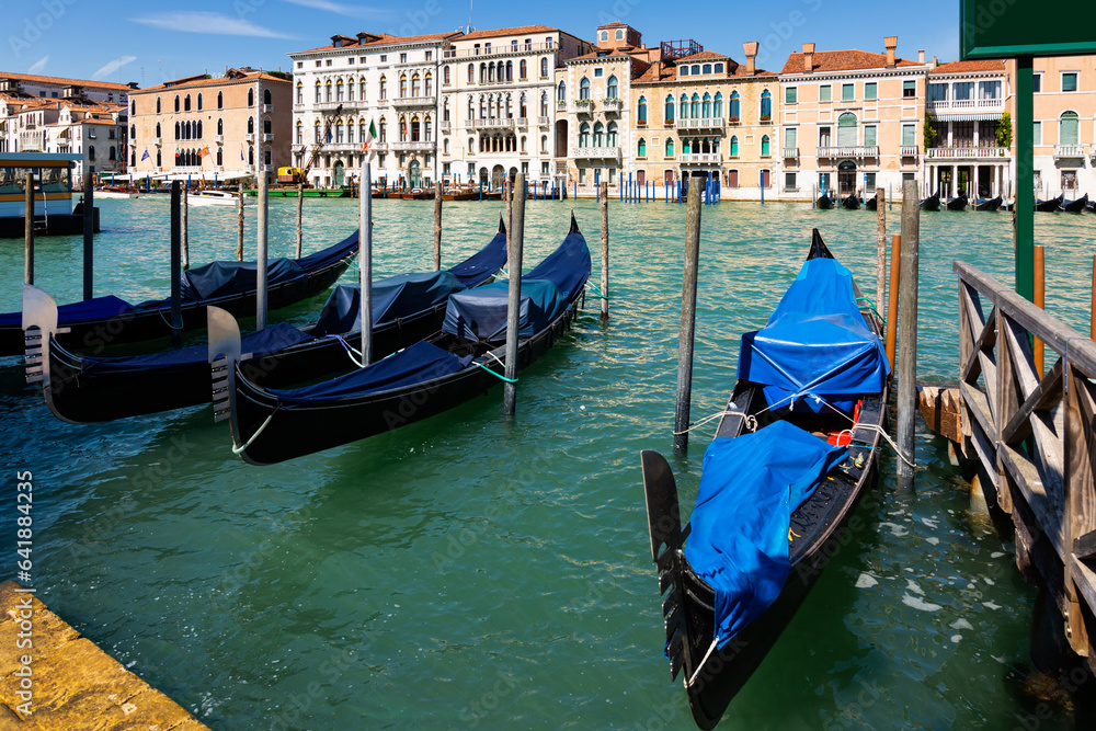 Traditional Venetian gondolas moored to pier in Grand Canal on background with old colorful architecture of central districts of Venice